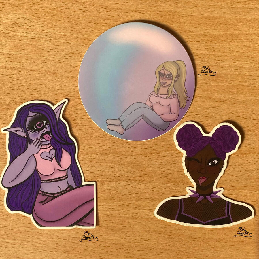 A picture of 3 vinyl stickers: A purple cyclops woman with her legs crossed & her tongue stuck out, a black girl with bright purple hair & piercings, sticking her tongue out & winking, and a circle sticker of a young tan woman sitting in a bubble.